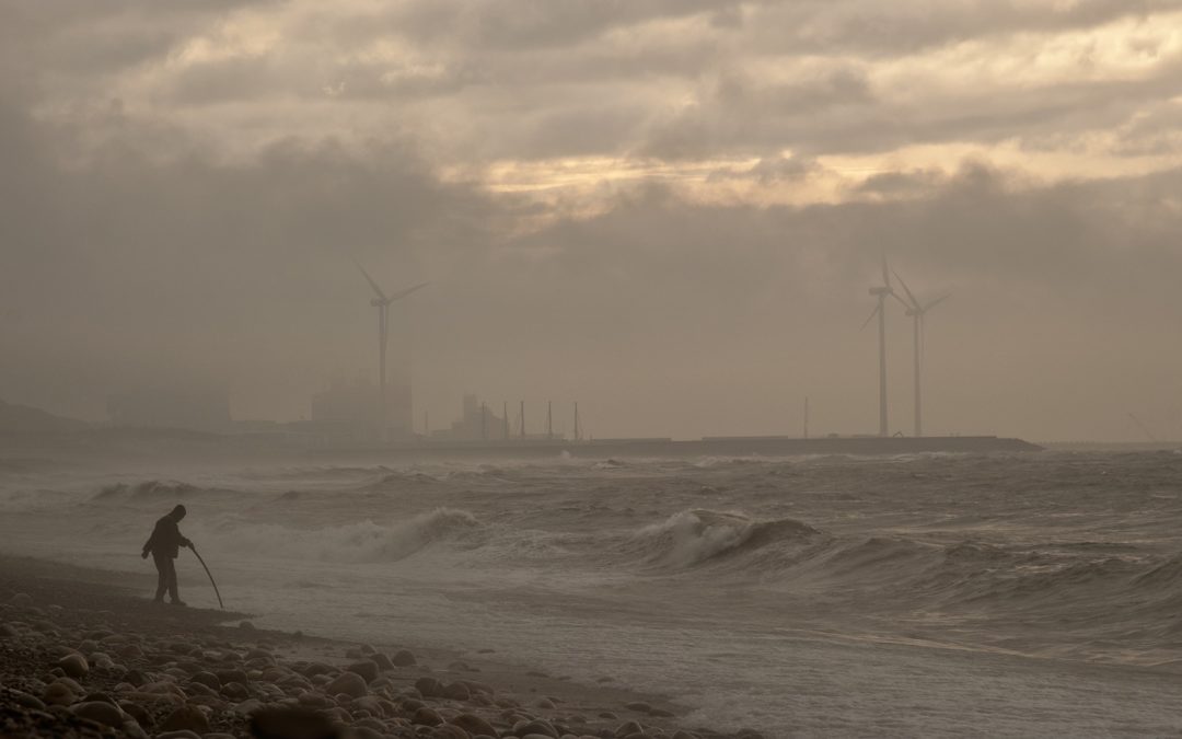 Man on beach during windstorm with windmills in the background